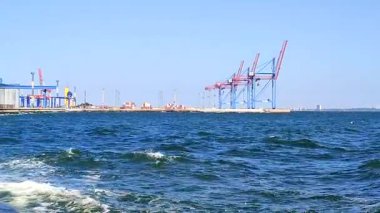 Liman. Güneşli bir günde liman manzarası. İskele vinçleri, nakliye için konteynır deposu ve deniz. İskele terminali, lojistik liman