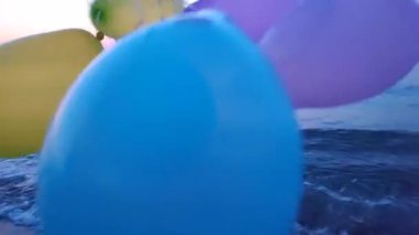 Şafak ve gün batımında denizin arka planında renkli şişme balonlar. Sahildeki kumlu kumsalda arka planda çok renkli balonlarla oynayan kişi. Eğlence eğlencesi