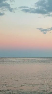 Denizde güzel bir gün batımı. Sakin mavi denizin yüzeyi, bulutlu mavi gökyüzü, ufuk çizgisi ve pembe günbatımı. Dikey