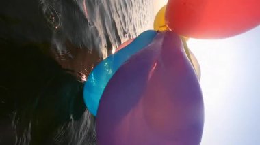 Gündoğumunda ve günbatımında deniz kıyısında bir sürü renkli balonla oynayan kişi. Güneş balonların arasından parlıyor. Rahatla ve eğlen. Yavaş çekim Dikey