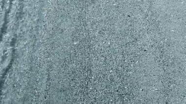 Güneşli bir günde, deniz kıyısının kumlu sahilinde, şeffaf, küçük deniz dalgaları. Temiz su, güneş parlaması ve yakın plan kumlu zeminde gölgeler. Doğal soyut arkaplan