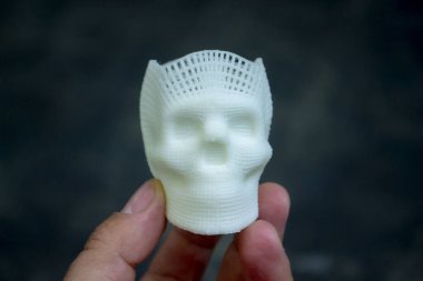 Elinde erimiş plastikten siyah zemin üzerine basılmış insan kafatasının küçük beyaz prototipini tutan kişi. Üç boyutlu model. Katkı teknolojisi. Modern yeni baskı endüstrisi.