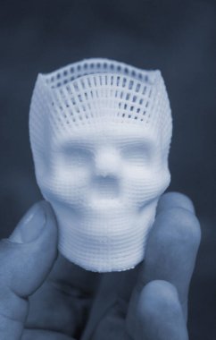 Elinde erimiş plastikten siyah zemin üzerine basılmış insan kafatasının küçük beyaz prototipini tutan kişi. Üç boyutlu model. Katkı teknolojisi. Baskı endüstrisi. Mavi renk