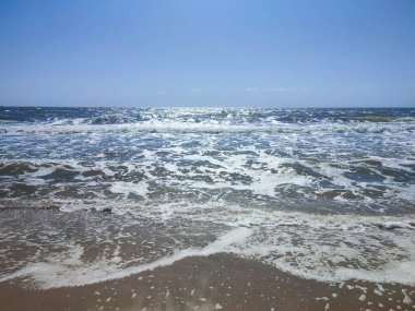 Beyaz köpüklü, şeffaf deniz dalgaları ve güneşli bir yaz gününde kumlu sahil sahilinde mavi gökyüzü. Deniz kıyısında. Kumsal. Doğa Doğal arkaplan