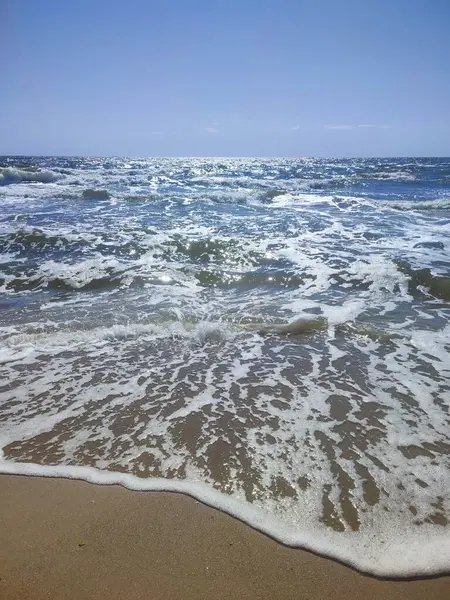 Beyaz köpüklü, şeffaf deniz dalgaları ve güneşli bir yaz gününde kumlu sahil sahilinde mavi gökyüzü. Deniz kıyısında. Kumsal. Doğa Doğal arkaplan