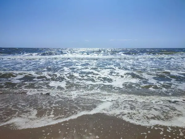 Beyaz köpüklü, şeffaf deniz dalgaları ve güneşli bir yaz gününde kumlu sahil sahilinde mavi gökyüzü. Deniz kıyısında. Kumsal. Doğa Doğal arkaplan