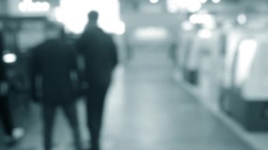 Binada yürüyen insanlar. Duvarları, zemini, tavan lambaları olan bir bina. İçerideki insanların siluetleri. Bir sürü insan yürüyor. Erkekler ve kadınlar uzun salonda. Sergi merkezi. Bulanık arkaplan