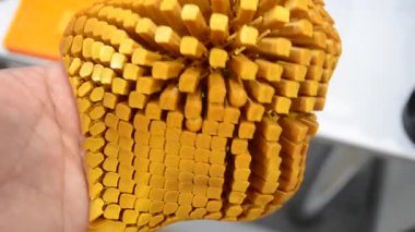 Elindeki 3D yazıcıya basılmış nesne. Model birçok küçük parçadan 3D yazıcı üzerinde oluşturuldu. Erimiş sarı plastikten yapılmış 3D yazıcıya basılmış. Plastik esnek model. FDM 3D yazıcı teknolojileri