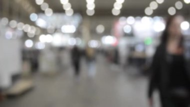 Binada yürüyen insanlar. Duvarları, zemini, tavan lambaları olan bir bina. İçerideki insanların siluetleri. Bir sürü insan yürüyor. Erkekler ve kadınlar uzun salonda. Sergi merkezi. Bulanık arkaplan