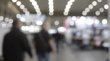 Binada yürüyen insanlar. Duvarları, zemini, tavan lambaları olan bir bina. İçerideki insanların siluetleri. Bir sürü insan yürüyor. Erkekler ve kadınlar uzun salonda. Sergi merkezi. Bulanık arkaplan