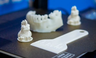 Beyaz plastikten yapılmış küçük beyaz figürler 3 boyutlu bir yazıcının çalışan yüzeyine yakın plan yazıcıdan basılmış. FDM. Konsept 3 boyutlu baskı. Katkı sağlayan modern yenilikçi teknolojiler