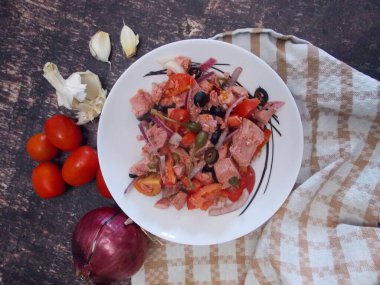 Soğanlı mavi yüzgeçli ton balığı salatası. Domates kapari ve sarımsak. Arka planda karanlık bir plaj yemeği.