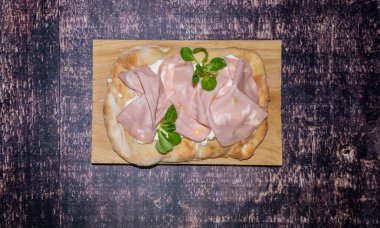 Roman pinsa, variant of the classic Italian pizza topped with mortadella, stracciatella and lamb's lettuce and pistachios