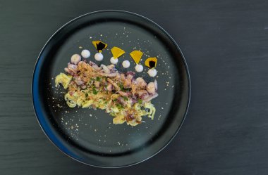 İtalyan aperatifi ahtapot, enginar ve siyah bir tabağa bottarga serpiştirilmiş.