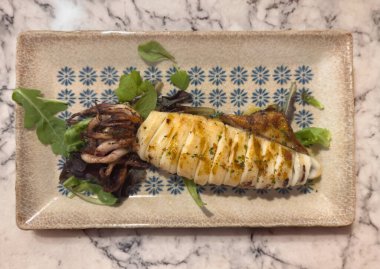 Rafta kalamar ve limon ve salata ile terbiye edilmiş dikdörtgen tabakta.