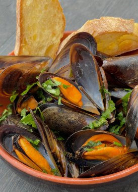 Maydanozla kaynatılmış midye çorbası çelik bir tencerede hafif arka planda sarımsak.