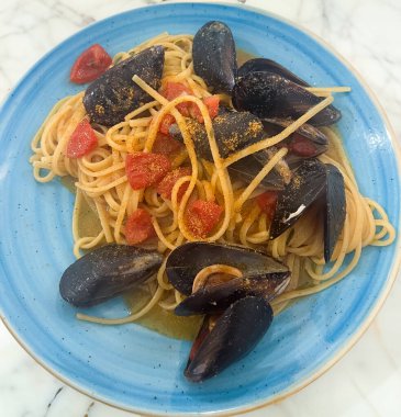 Mavi tabakta baharatlı domates püresi ve beyaz arka planda midyeli spagetti.