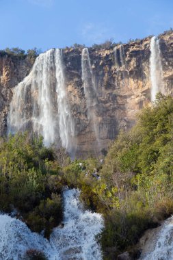 Scenic view of a waterfall flowing down a rocky cliff surrounded by a dense forest, creating a breathtaking natural landscape clipart