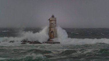 Ocean waves crashing against a lighthouse during a heavy storm clipart