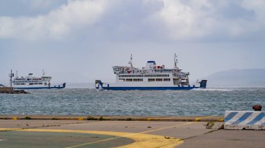 Dalgalı bir denizde yelken açan feribot. Arka planda bir rüzgar türbini çiftliği var.
