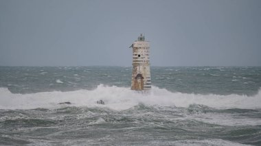 Beyaz ve siyah çizgili deniz feneri fırtınalı deniz dalgalarıyla çevrili.