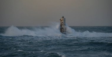 Beyaz ve siyah çizgili deniz feneri fırtınalı deniz dalgalarıyla çevrili.