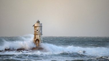 Beyaz ve siyah çizgili deniz feneri fırtınalı deniz dalgalarıyla çevrili.