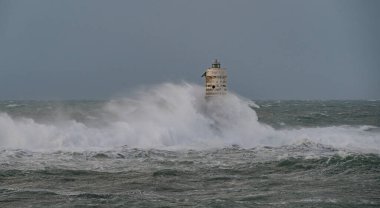 Beyaz ve siyah çizgili deniz feneri fırtınalı deniz dalgalarıyla çevrili.