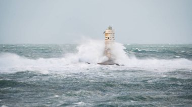 Beyaz ve siyah çizgili deniz feneri fırtınalı deniz dalgalarıyla çevrili.
