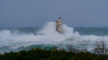 Ocean waves crashing against a lighthouse during a powerful storm at sea clipart