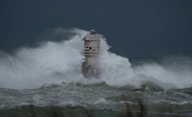 Ocean waves crashing against a lighthouse during a powerful storm at sea clipart