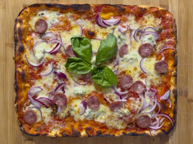 Square pizza cooked in a pan with tomato, mozzarella, tropea red onions, gorgonzola cheese and sausage, resting on a cutting board clipart