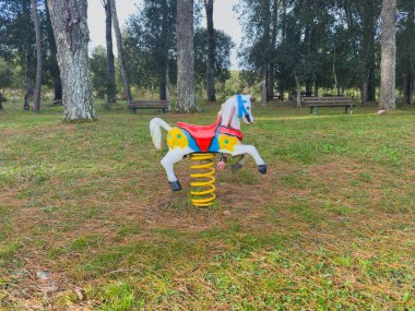 Renkli at binicisi halka açık bir parkta oturuyor, çocukların eğlenmesi için hazır.