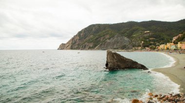 Renkli şemsiyeli, tarihi villalı ve Cinque Terre 'deki yeşil tepeli Monterosso sahili manzarası.