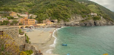 Renkli şemsiyeli, tarihi villalı ve Cinque Terre 'deki yeşil tepeli Monterosso sahili manzarası.