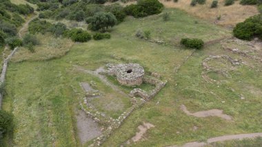 İtalya 'nın Sardunya kentindeki yeşil çimenler ve antik taş kalıntılarıyla çevrili Nuragic kutsal kuyu yapısının havadan görünüşü