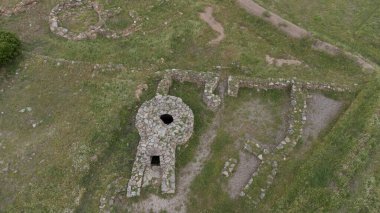 İtalya 'nın Sardunya kentindeki yeşil çimenler ve antik taş kalıntılarıyla çevrili Nuragic kutsal kuyu yapısının havadan görünüşü