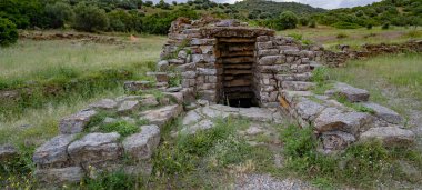 İtalya 'nın Sardunya kentindeki yeşil çimenler ve antik taş kalıntılarıyla çevrili Nuragic kutsal kuyu yapısının havadan görünüşü