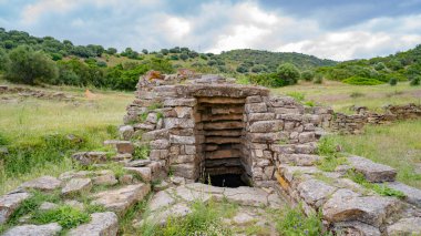İtalya 'nın Sardunya kentindeki yeşil çimenler ve antik taş kalıntılarıyla çevrili Nuragic kutsal kuyu yapısının havadan görünüşü