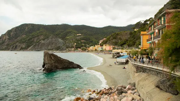 Renkli şemsiyeli, tarihi villalı ve Cinque Terre 'deki yeşil tepeli Monterosso sahili manzarası.
