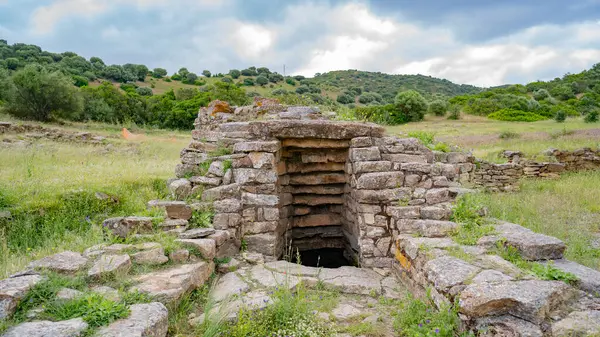 İtalya 'nın Sardunya kentindeki yeşil çimenler ve antik taş kalıntılarıyla çevrili Nuragic kutsal kuyu yapısının havadan görünüşü