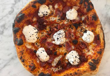 Üzeri burrata, salam, domates sosu ve siyah kırıntılarla kaplı zanaatkar pizza.