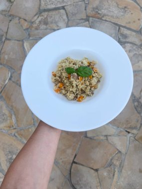 Beyaz tabakta servis edilen taze fesleğenle süslenmiş renkli kuskus..