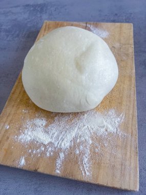 Taze pizza hamuru topu un ahşap tahtada dinleniyor, yuvarlanmaya hazır.
