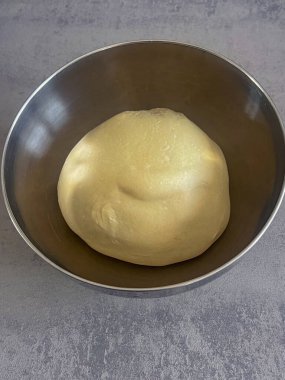 Pürüzsüz pizza hamuru kâsede dinleniyor, ev yapımı pişirme için hazır.