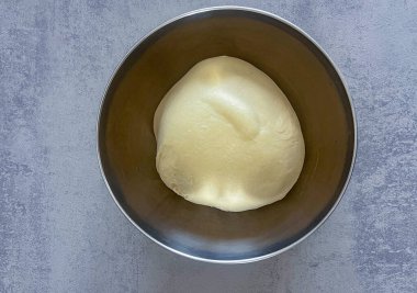 Pürüzsüz pizza hamuru kâsede dinleniyor, ev yapımı pişirme için hazır.