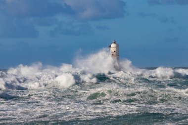 Şiddetli fırtına ve gri gökyüzü altında yükselen dalgalar deniz fenerine çarpıyor.