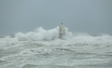 Şiddetli fırtına ve gri gökyüzü altında yükselen dalgalar deniz fenerine çarpıyor.