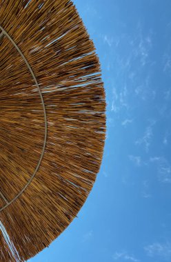 Mavi gökyüzüne karşı altından çekilmiş doğal saman plaj şemsiyesi.