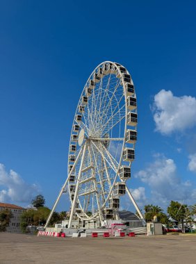 Parlak güneş ışığı ve bulutlarla mavi gökyüzüne doğru yükselen uzun bir dönme dolap.